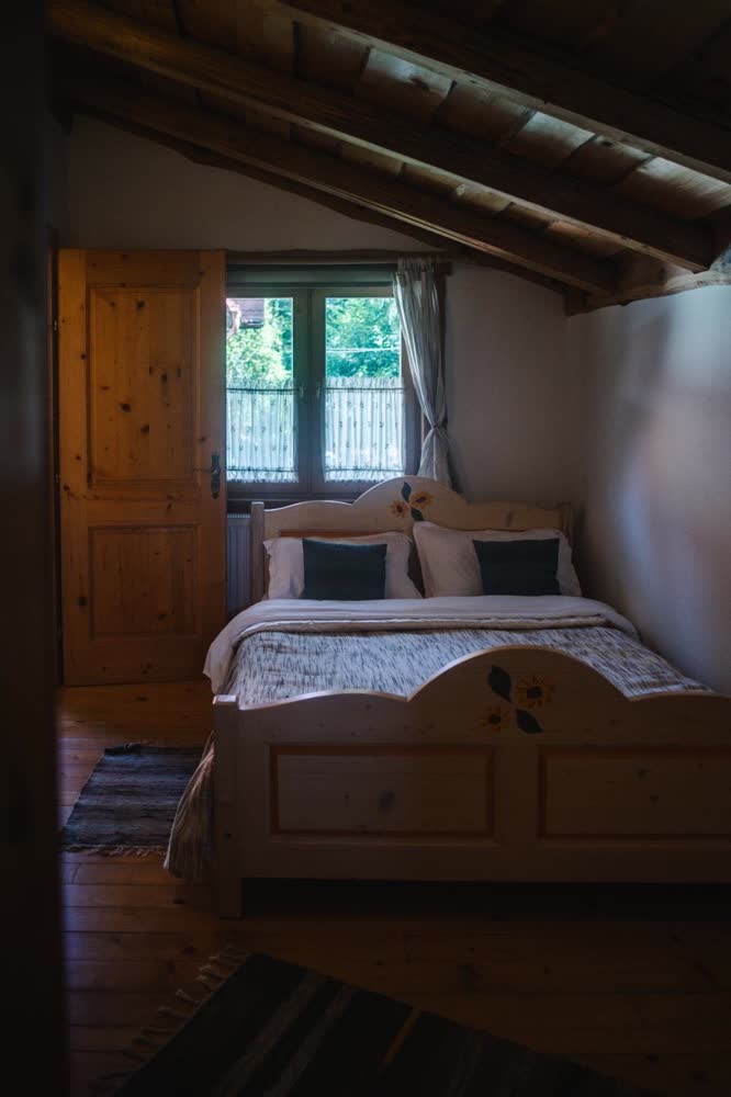 Dormitor la Cabana Bendis — pat de lemn masiv, la fereastră.